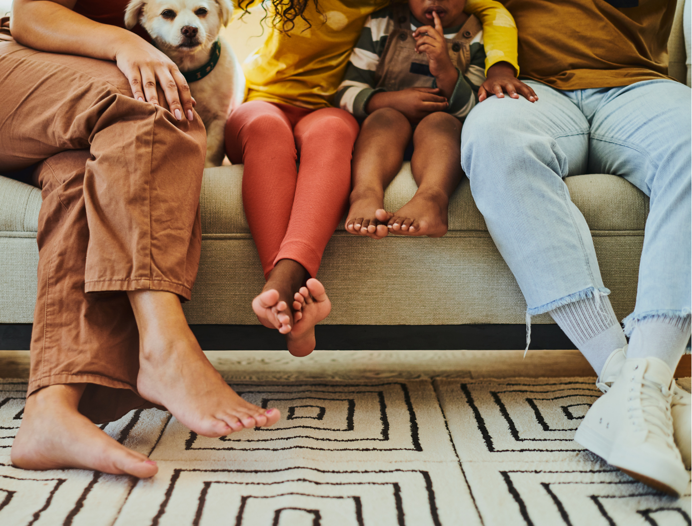 A family of four and their dog sitting together on a couch, cropped to show their legs and feet